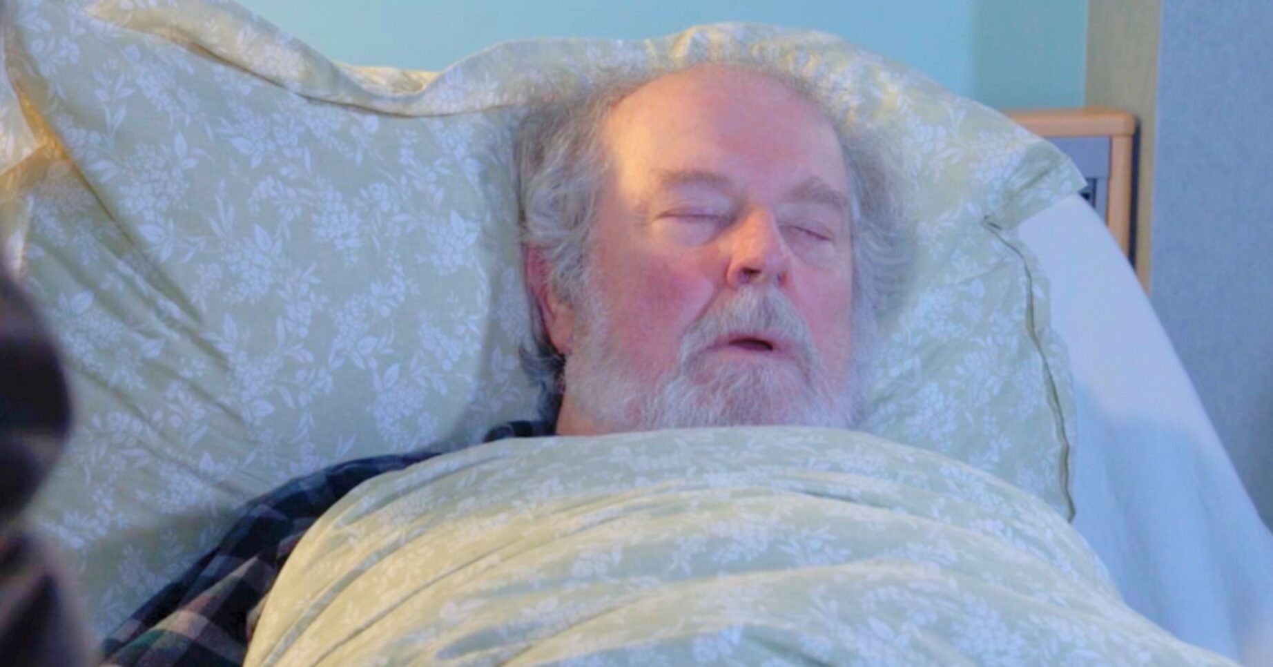 Julie sitting by Nigel's bed as he sleeps