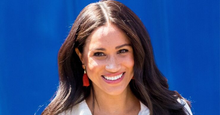 Meghan Markle smiling in front of blue background
