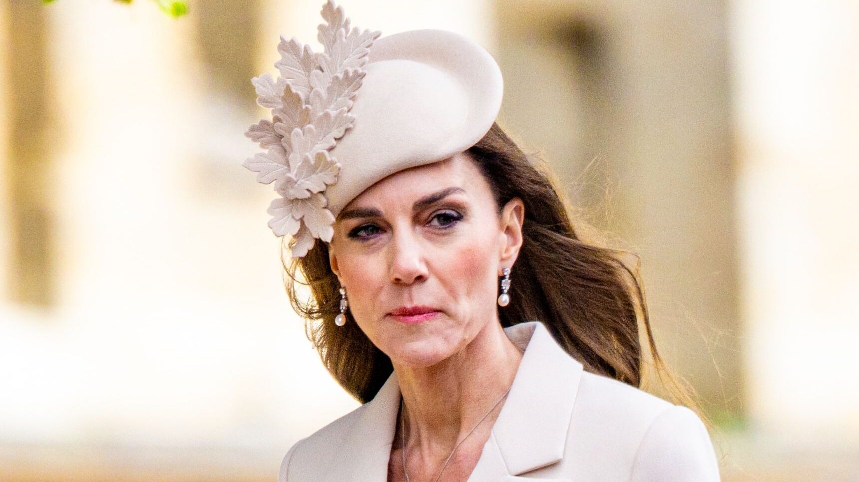 Princess Kate Middleton wearing a cream, floral hat with a serious expression