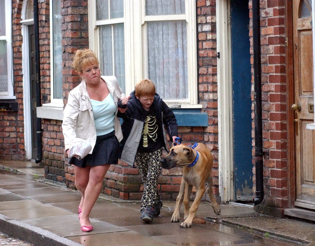 Editorial use only. Exclusive - Premium Rates Apply. Call your Account Manager for pricing. Mandatory Credit: Photo by ITV/REX/Shutterstock (710618lb) 'Coronation Street' TV - 2004 - After Janice's ultimatum Les has no choice but to send Chesney on his way. A furious Cilla grabs him by the hand and drags him down the street with Schmeichel in tow. Cilla Brown [Wendi Peters], Chesney Brown [Sam Aston] and Schmeichel [Great Dane]. ITV ARCHIVE