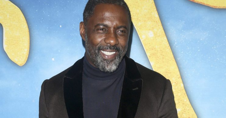 Idris Elba smiling wearing a dark jacket and polo neck