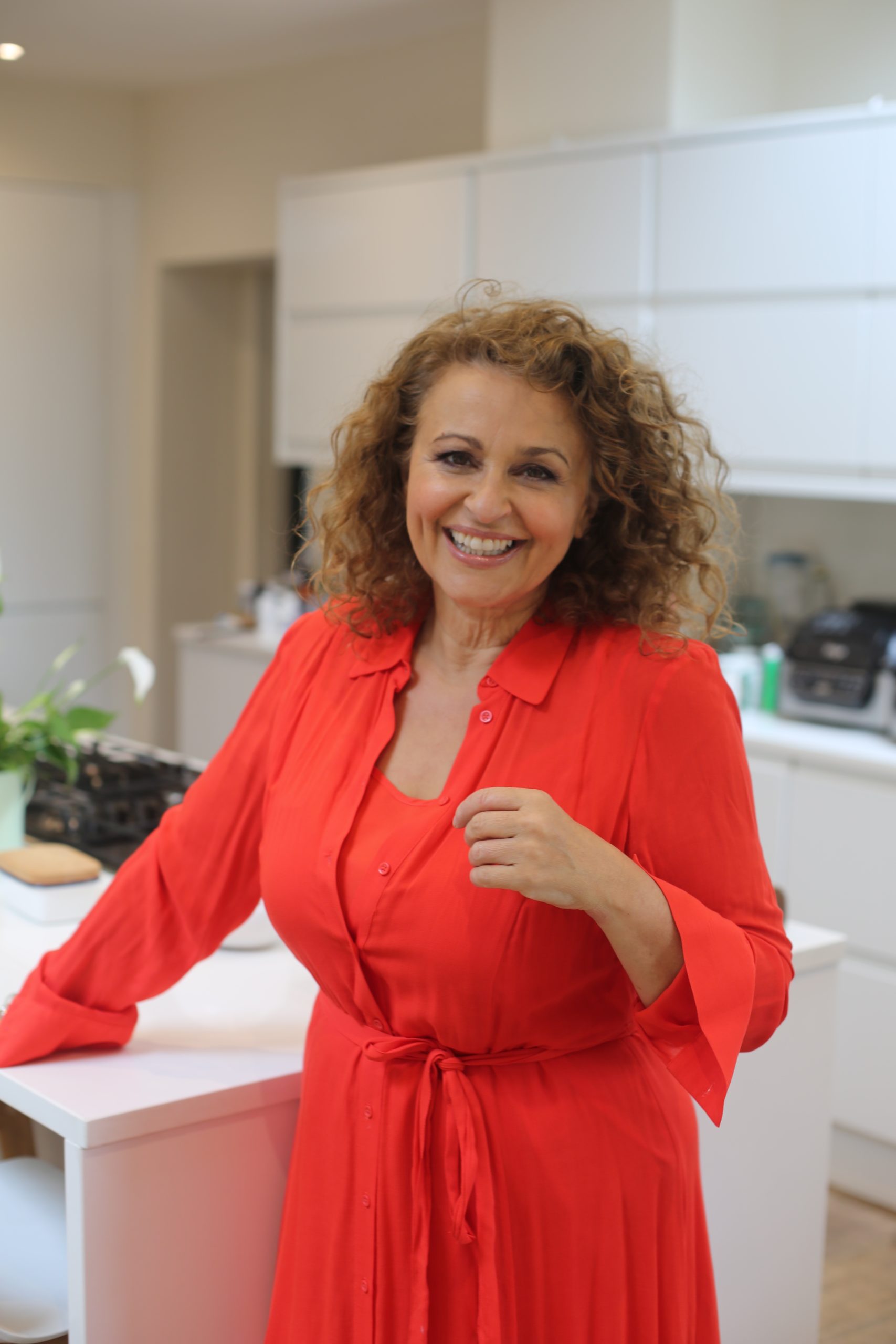 Nadia Sawalha posing ina red dress in her kitchen