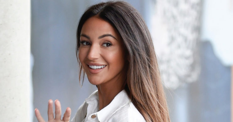 Michelle Keegan waving in a white blouse