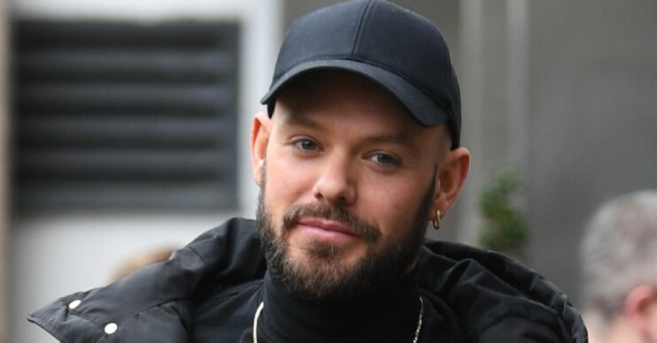 John Whaite smiles wearing a black cap