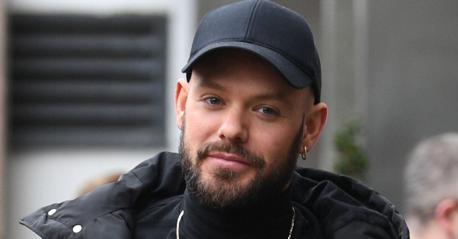 John Whaite smiles wearing a black cap