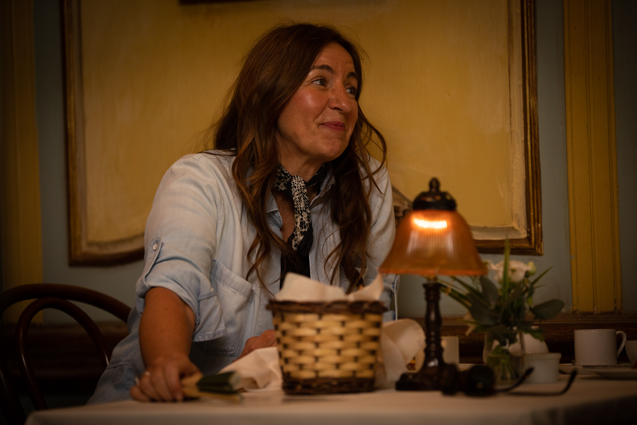 Kirsty Bushell as Sylvie in Murder in Provence smiling at a table in a dimly lit room