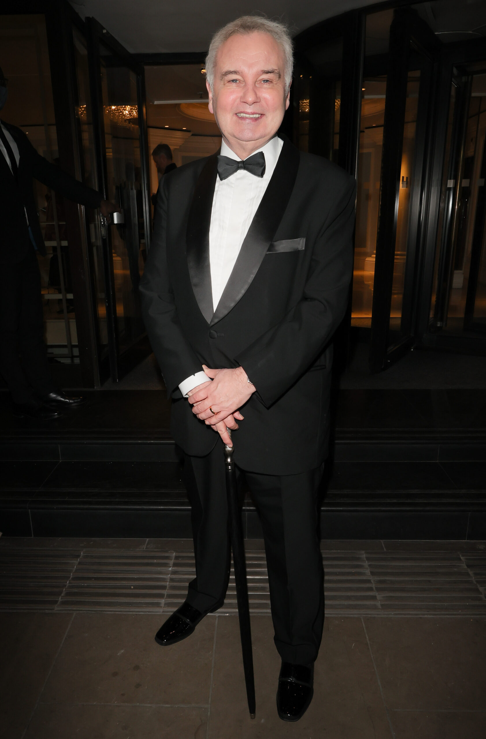 Eamonn Holmes wearing a tuxedo holding his walking stick, smiling for the camera