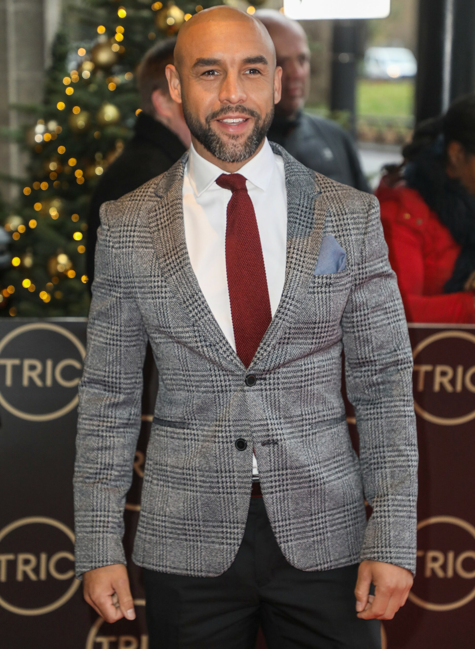Alex Beresford smiles in grey blazer and red tie at the TRIC Awards Christmas Lunch 2019
