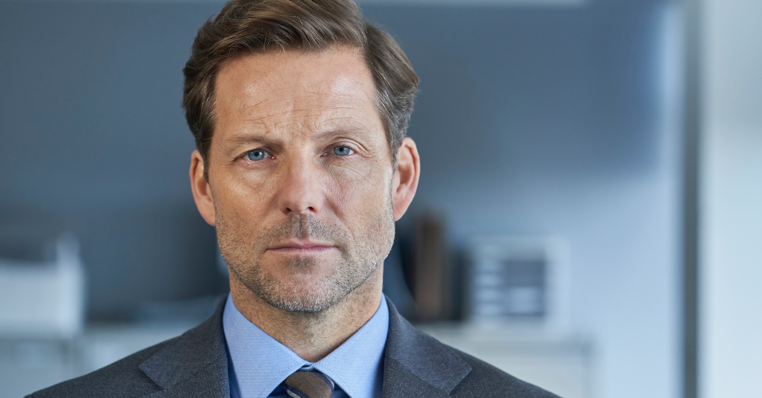 Jamie Bamber in a grey suit looking to camera