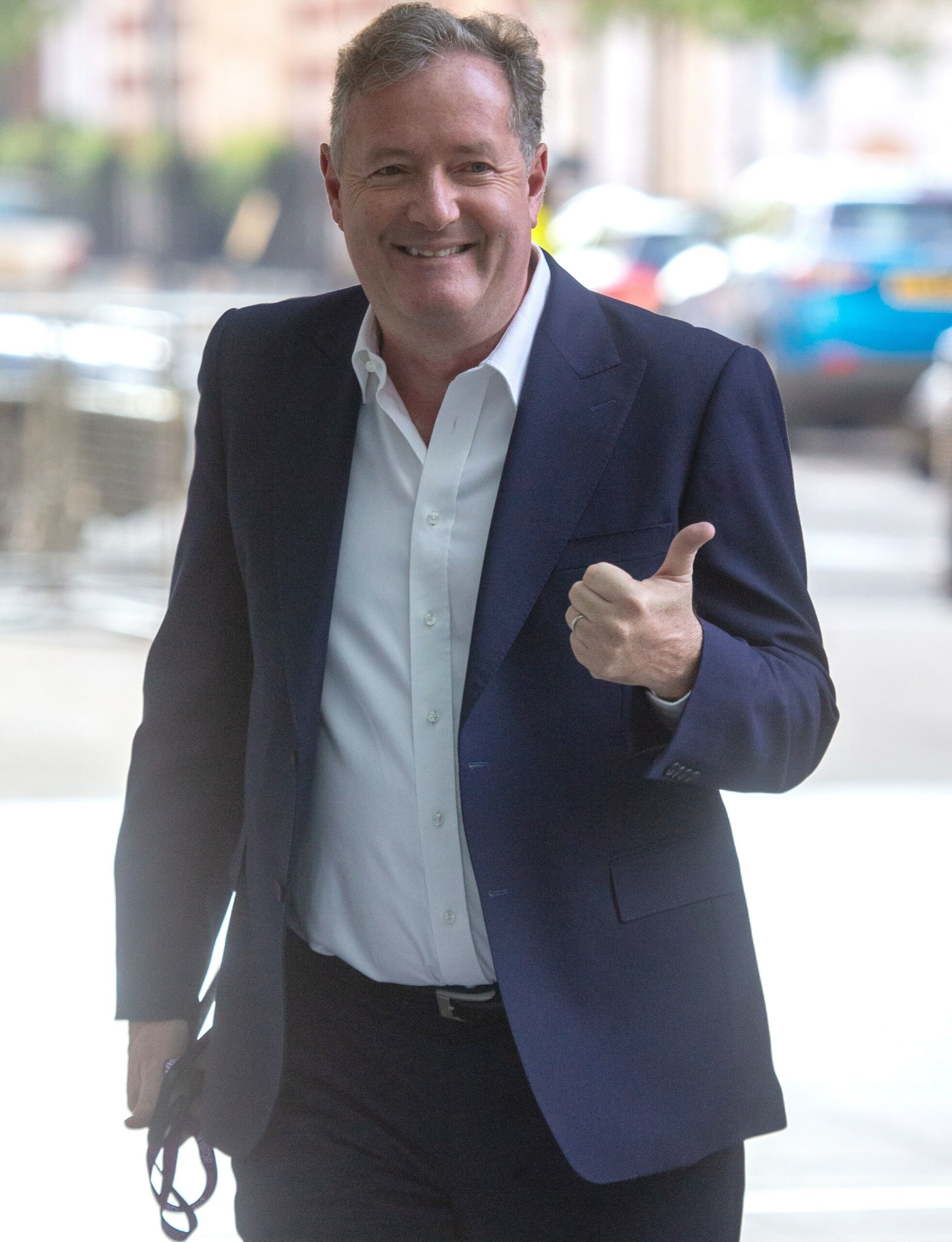 Piers Morgan smiles and puts thumbs up in suit during outing