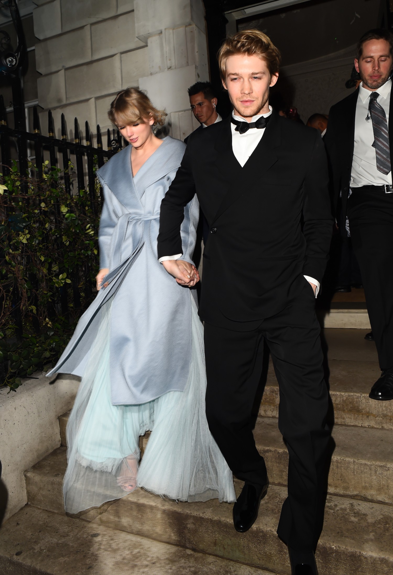Joe Alwyn and Taylor Swift smiling as they walk down concrete steps