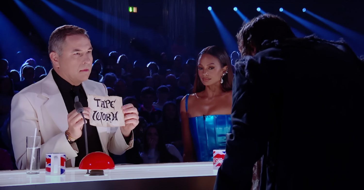 David Walliams holding up a piece of paper that reads 'tape worm' on Britain's Got Talent. Alesha Dixon sits next to him looking wary