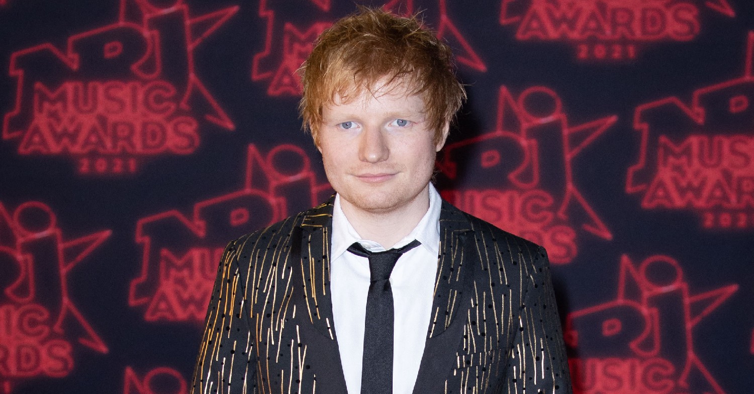 Ed Sheeran, smiling, in a suit on the red carpet 