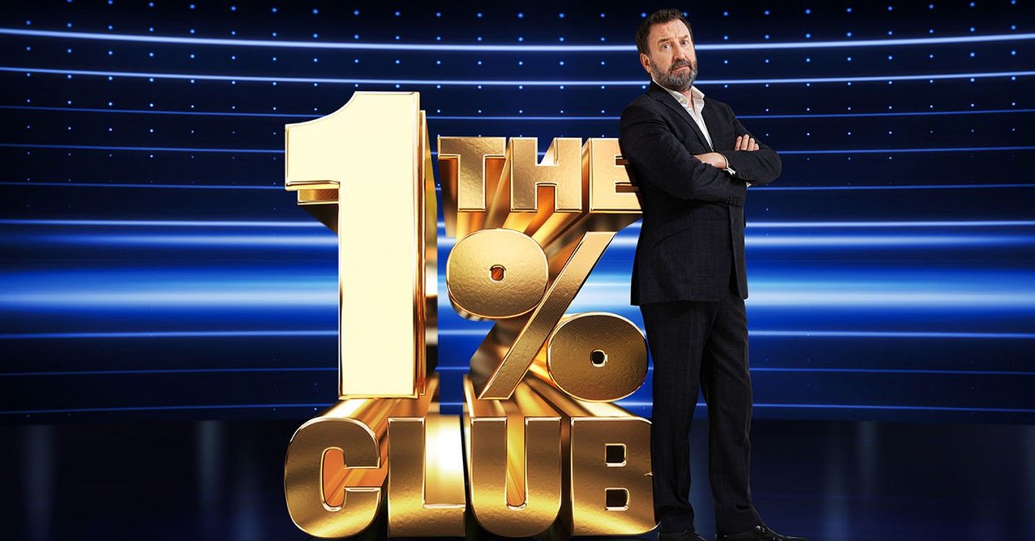 Lee Mack standing against The 1% Club logo