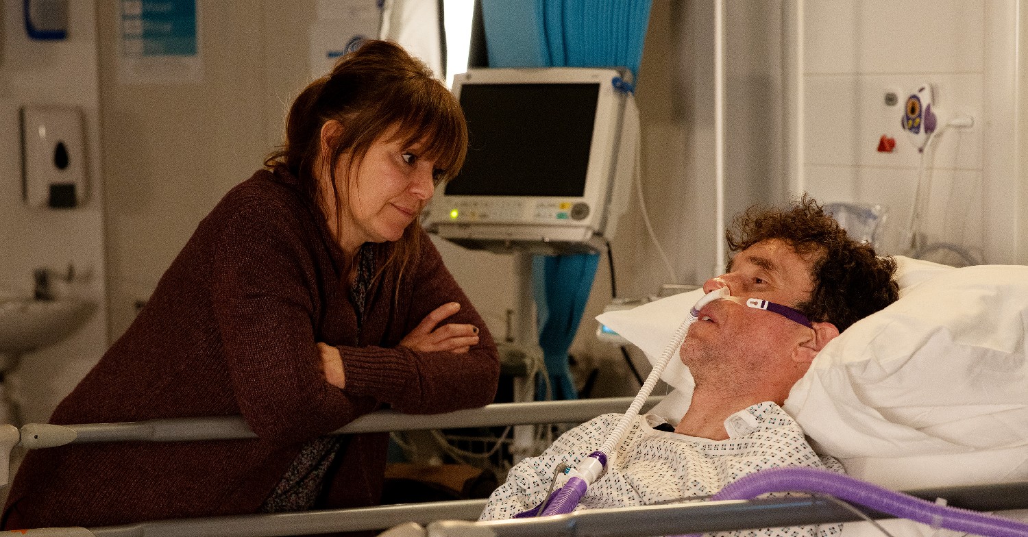 Marlon in hospital with tubes in him, with Rhona by his side (Credit: ITV)