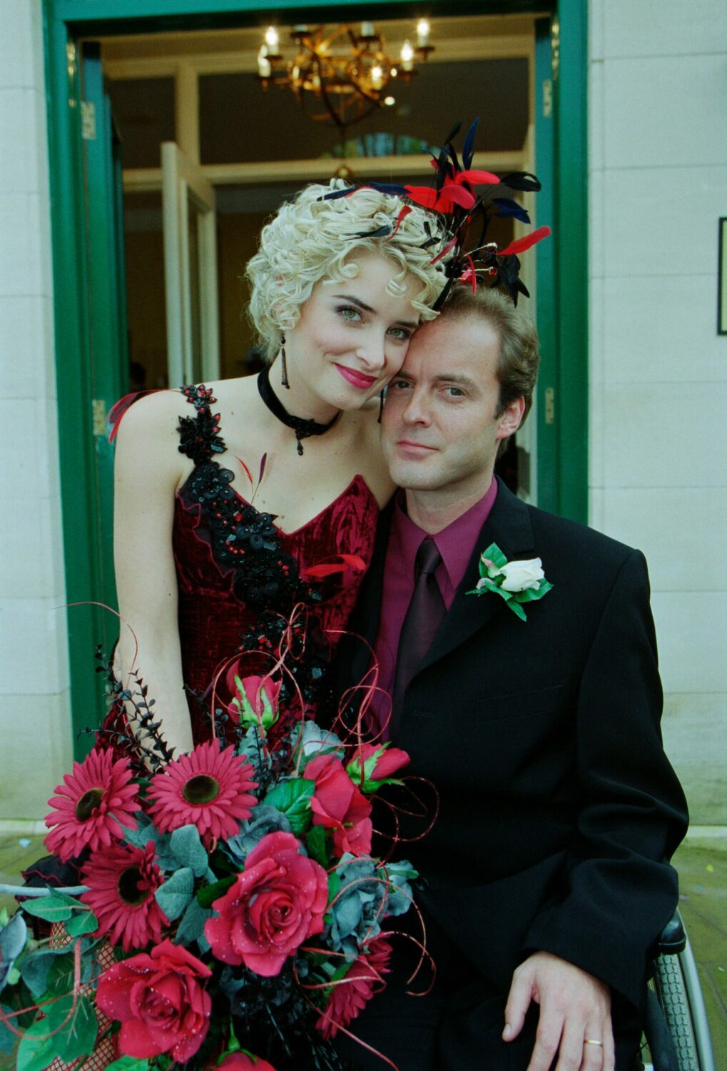 Charity Dingle in a dark red dress sits on her groom Chris's knee on their wedding day