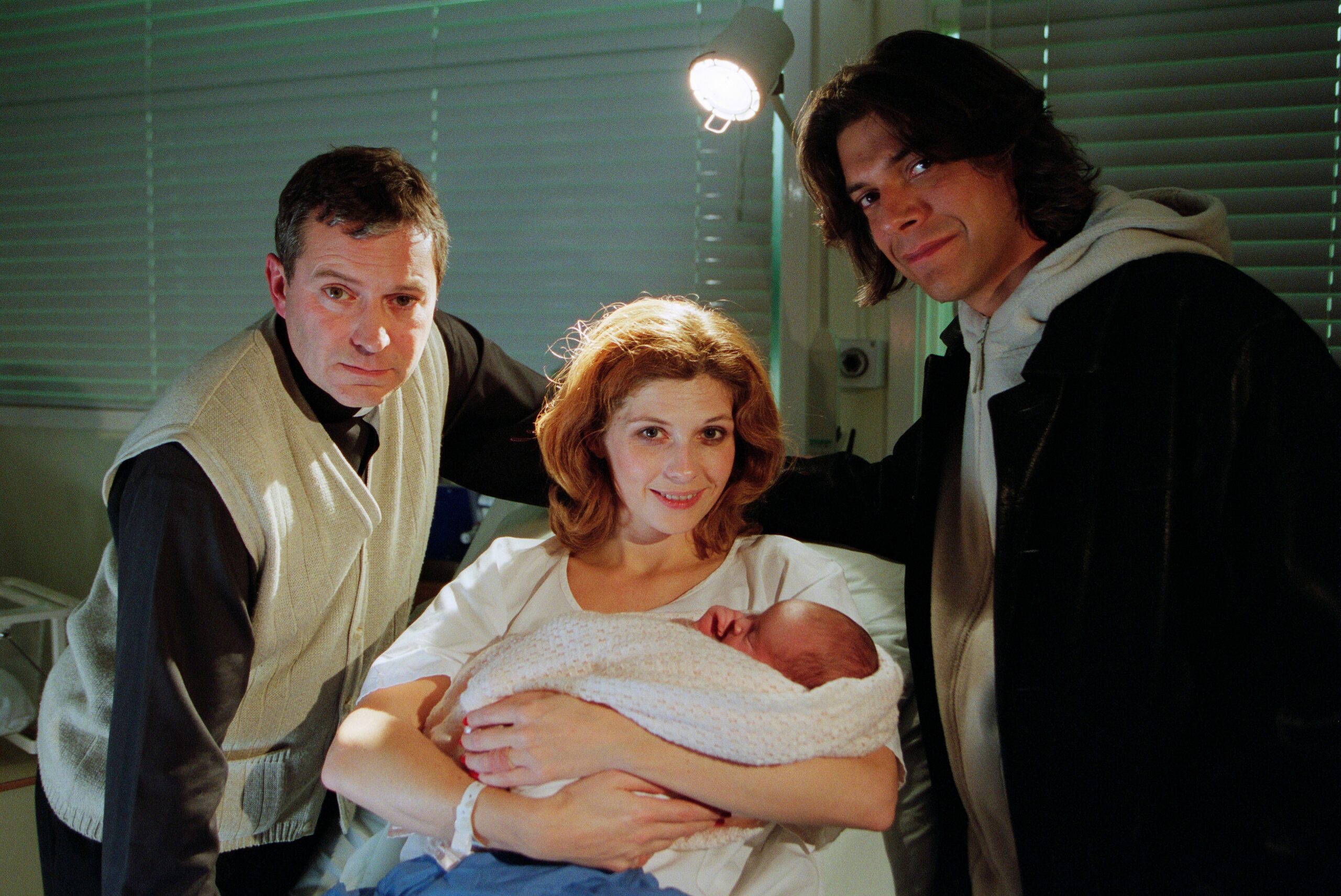 Bernice cradles baby Gabby while Carlos and Ashley stand either side of the bed