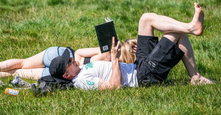One person reads and another sunbathes in the hot weather in the UK