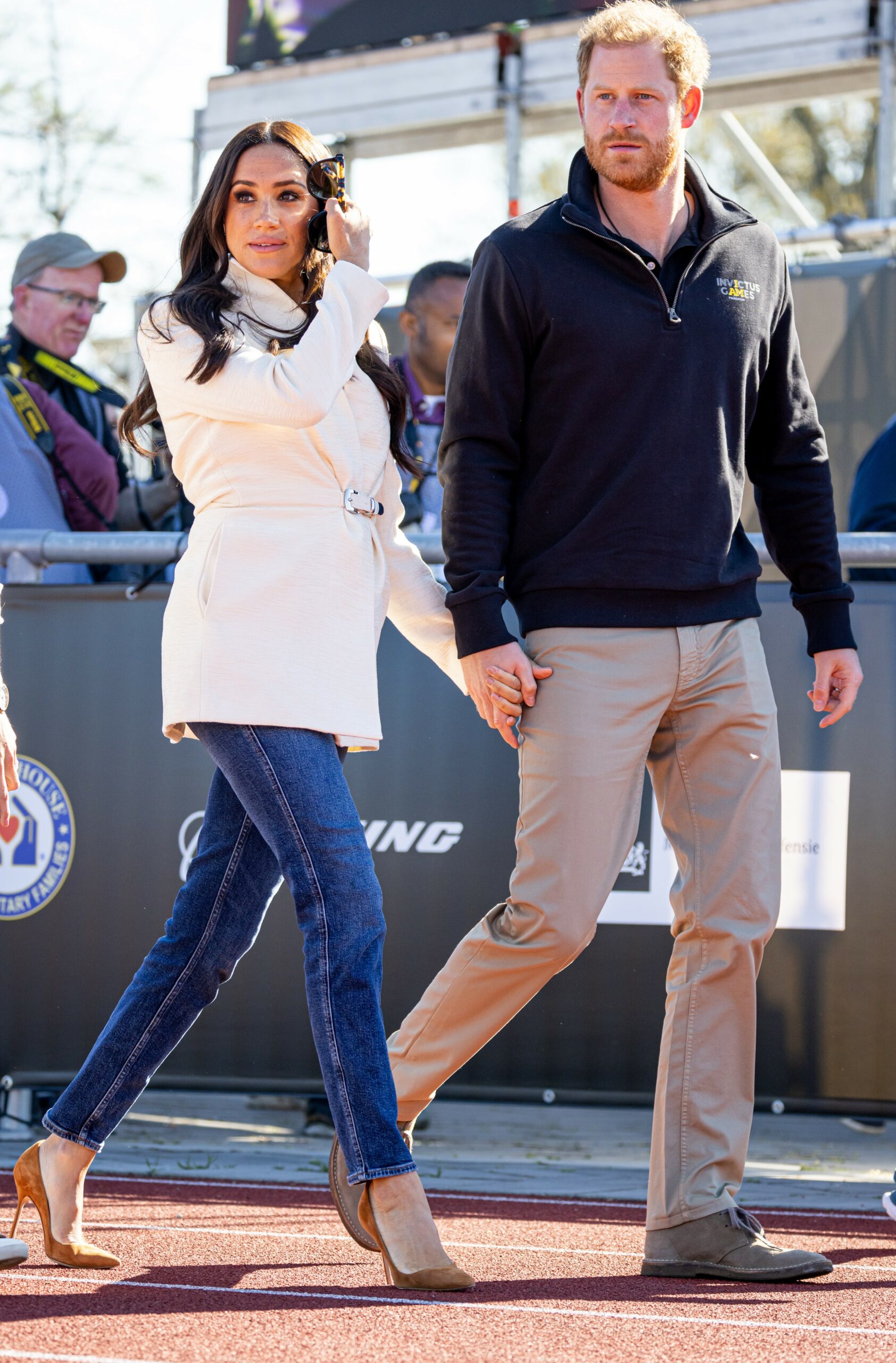 Meghan Markle and Prince Harry holding hands and looking towards cameras at Invictus Games
