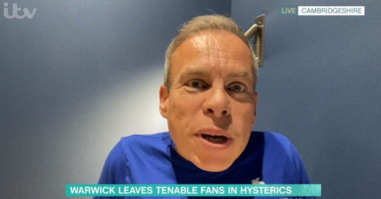Tenable host Warwick Davis in blue t-shirt while speaking to camera 