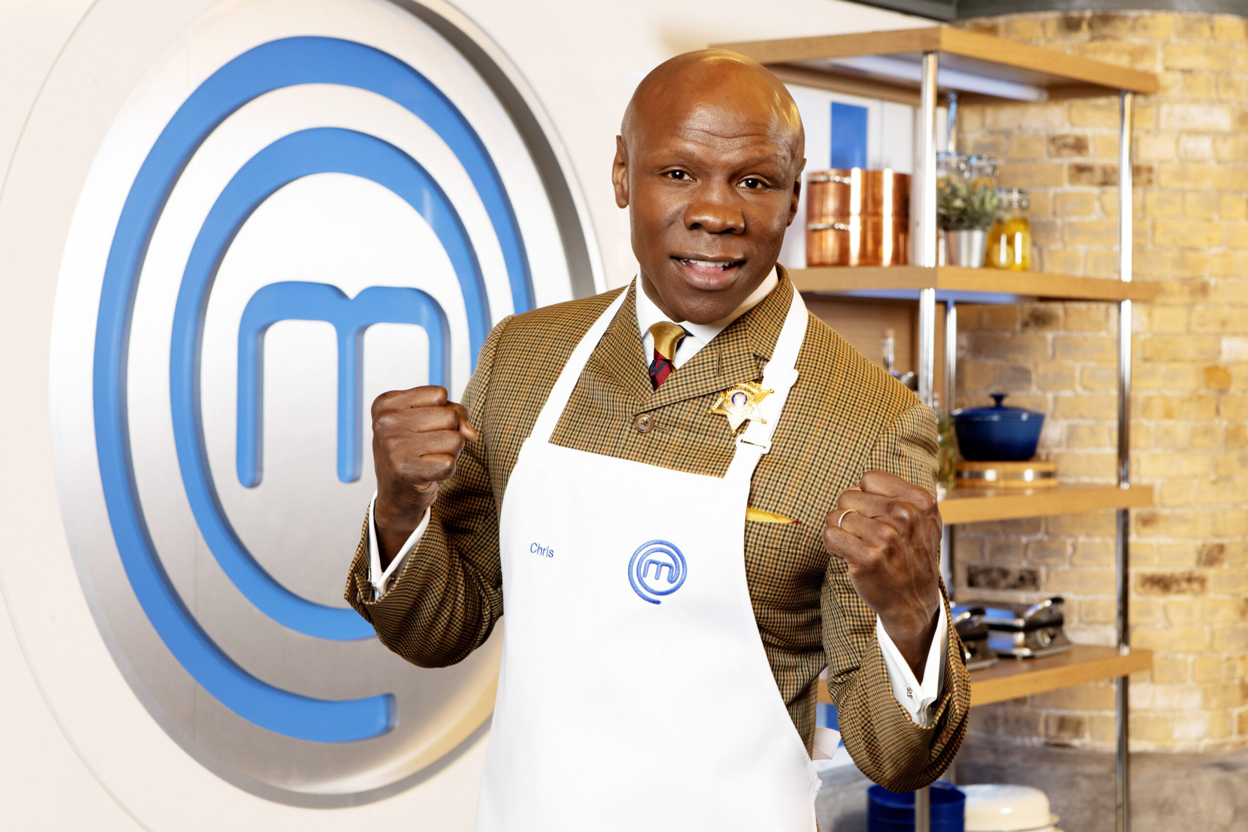 Chris Eubank poses with fists raised with Masterchef background and apron on