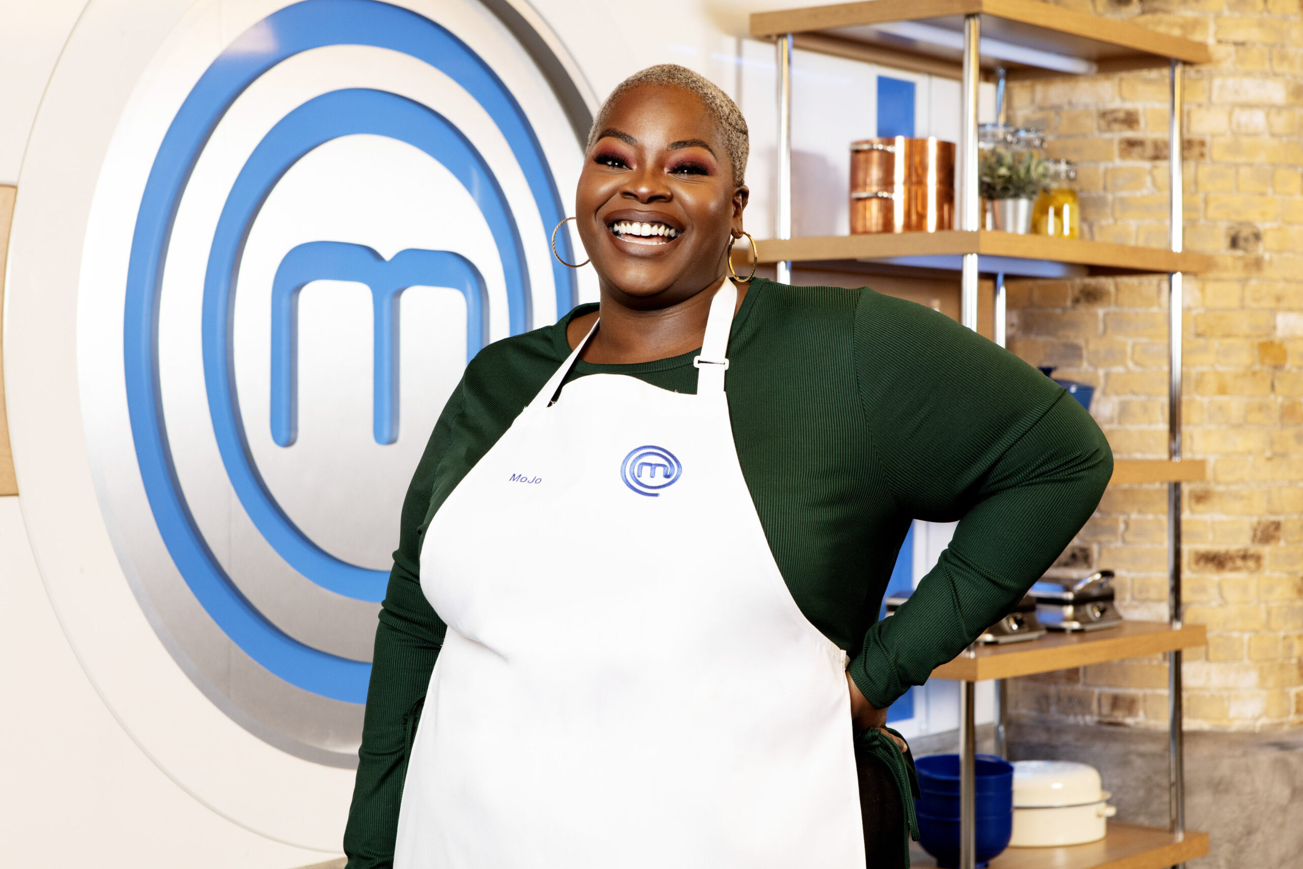 Queen Mojo poses with her hand on her hip in Celebrity Masterchef apron