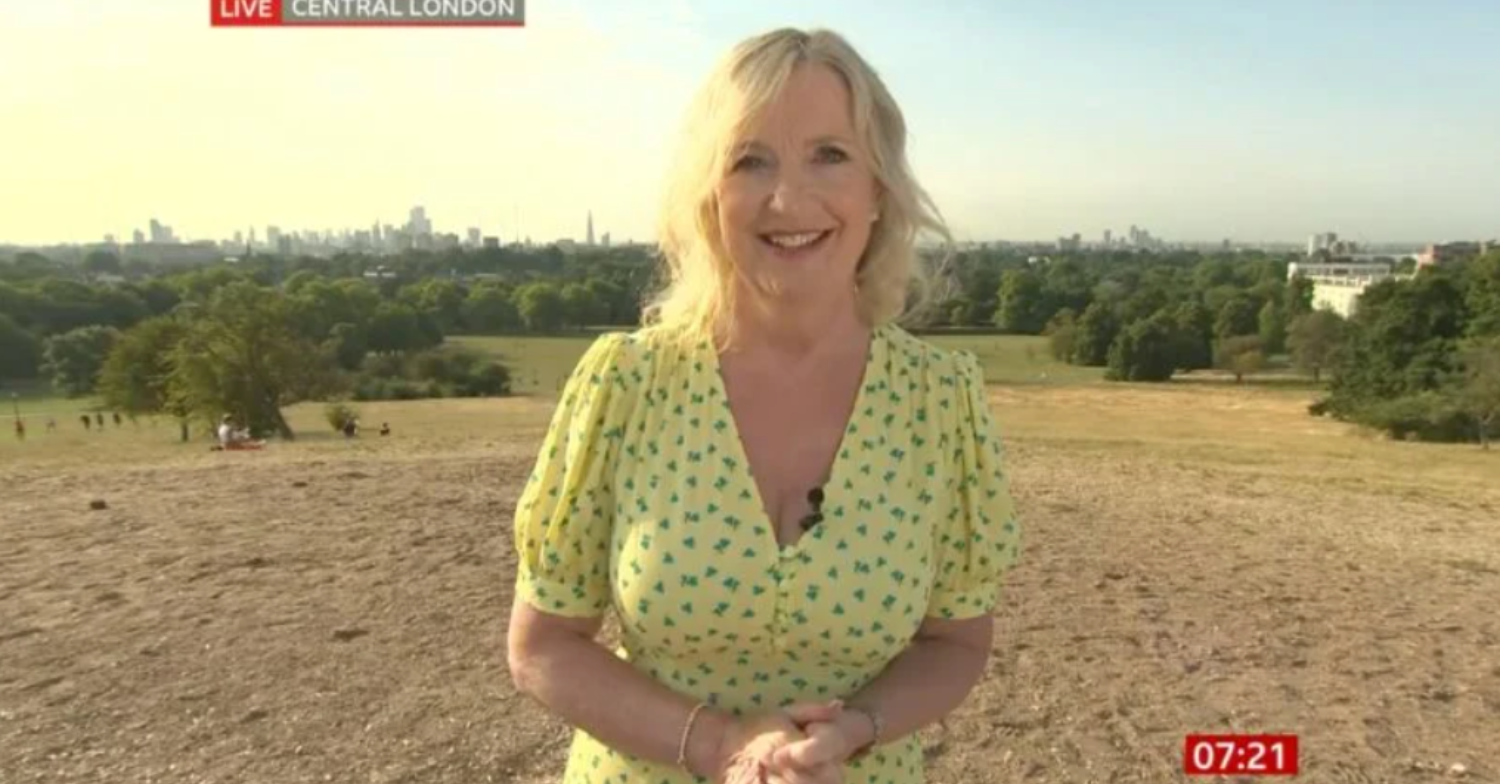 Carol Kirkwood wearing a yellow dress presenting from a field