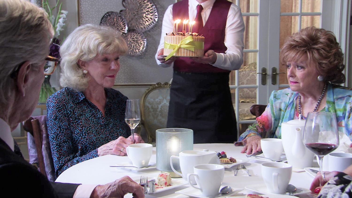 Audrey Roberts looks glum as Rita Tanner concerned while a cake is brought out with candles