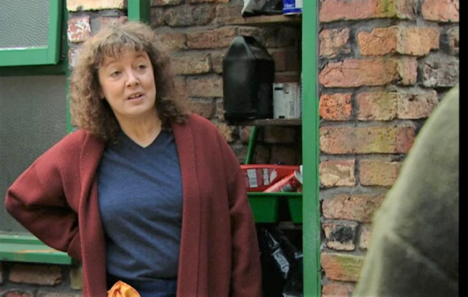 Edna Miller tries to smile with her hand on her hip in Coronation Street