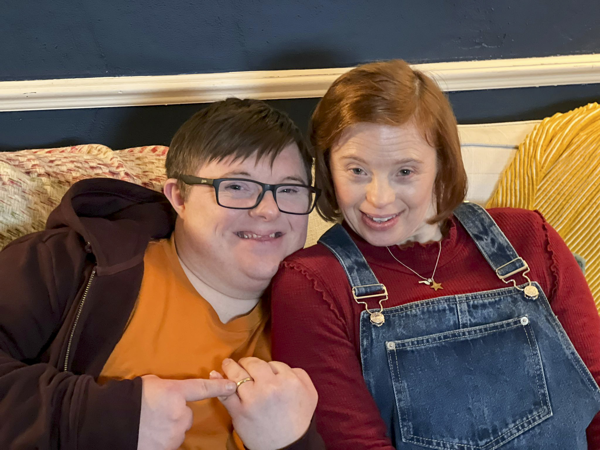 Leon Harrop as Ralph and Sarah Gordy as Katie in Ralph & Katie cuddle up on a sofa together as they smile