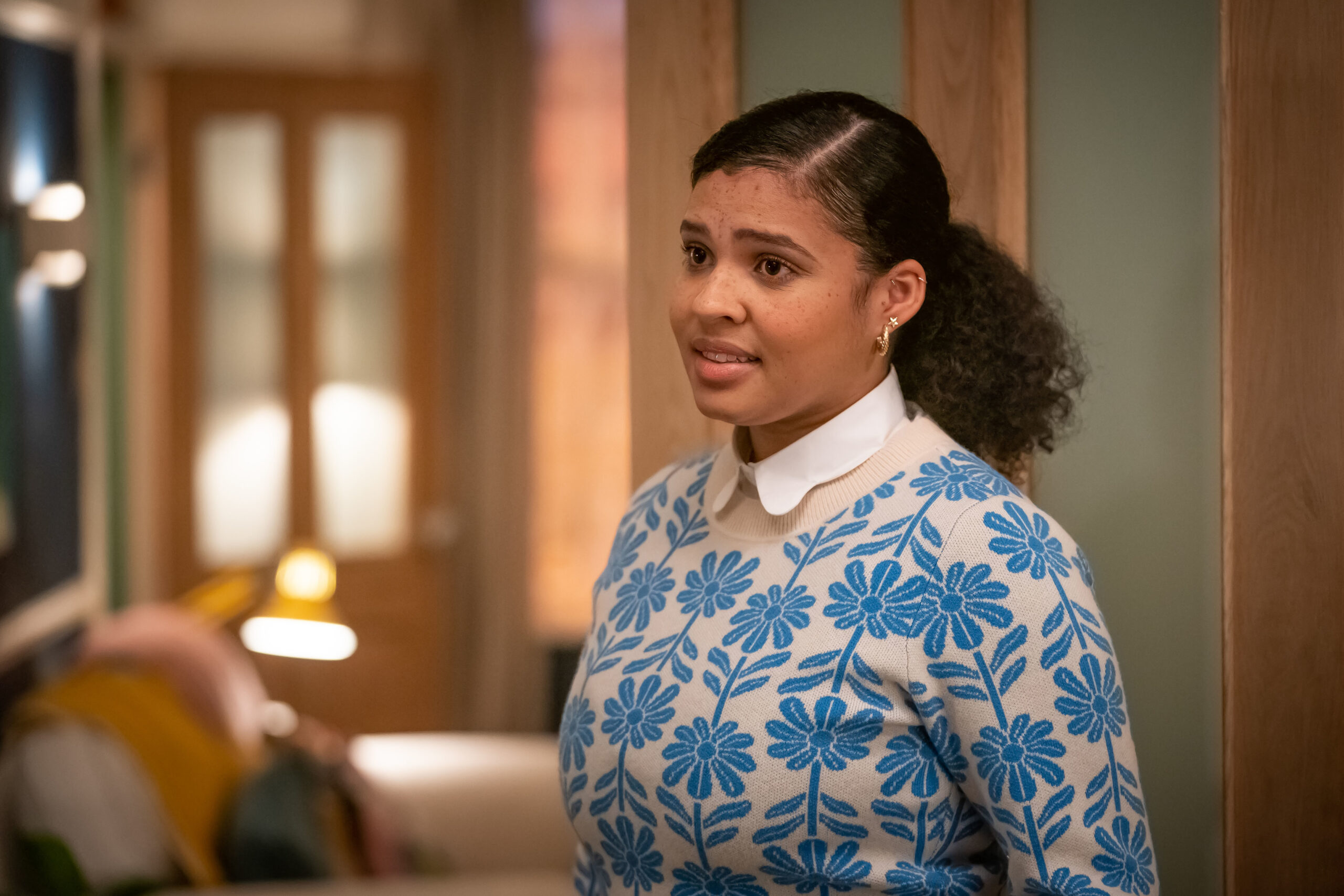 Jamie Marie Leary as Emma in Ralph & Katie, she stands in ralph and katies home as she smiles in a blue shirt