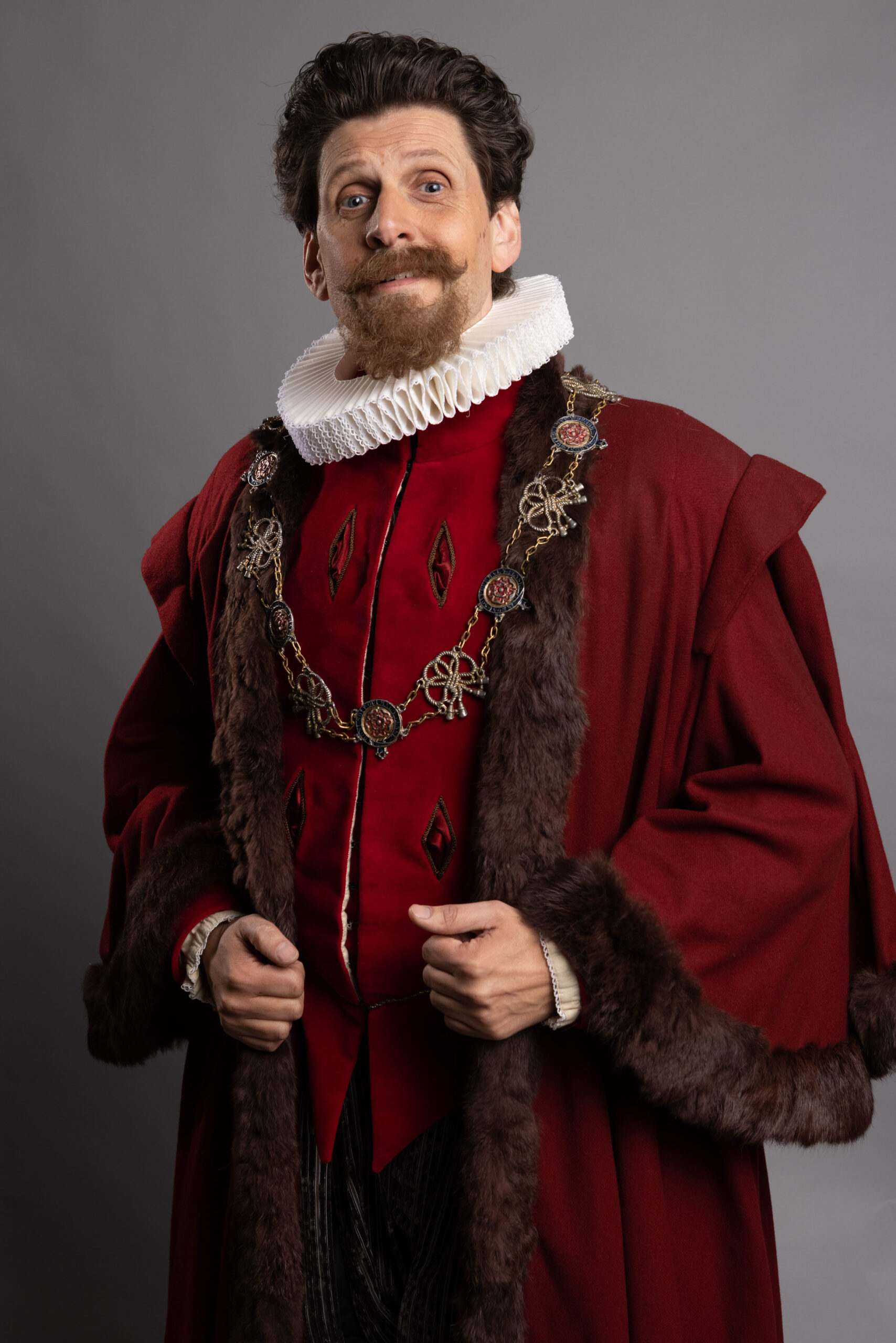 Larry Rickard as Humphrey in Ghosts, he is Elizabethan era robes and smiles into the camera