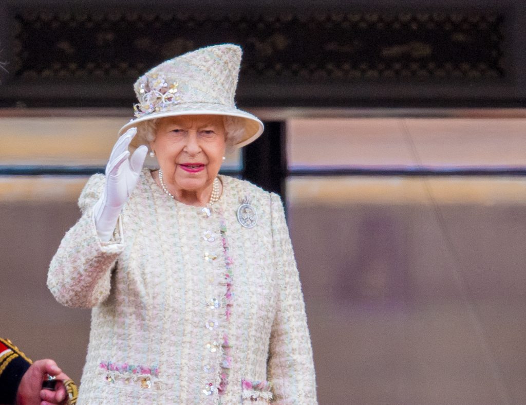 Queen Elizabeth II waves as she wears a white jacket and hat