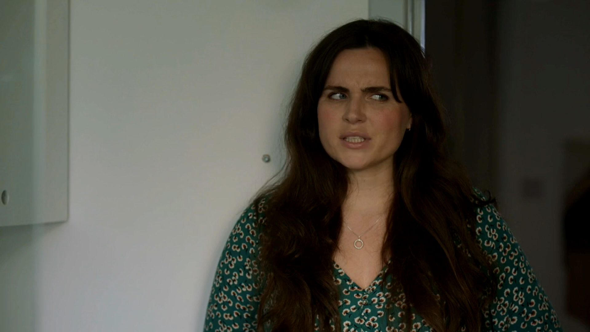 Emer Kenny as River Wilde in Karen Piere, she looks to the right in a green dress 
