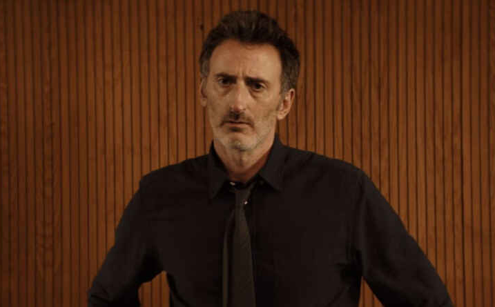 Andy Gathergood as Paul Rabbit in Professor T, he stands with a suit on with a dis-apporving look on his face