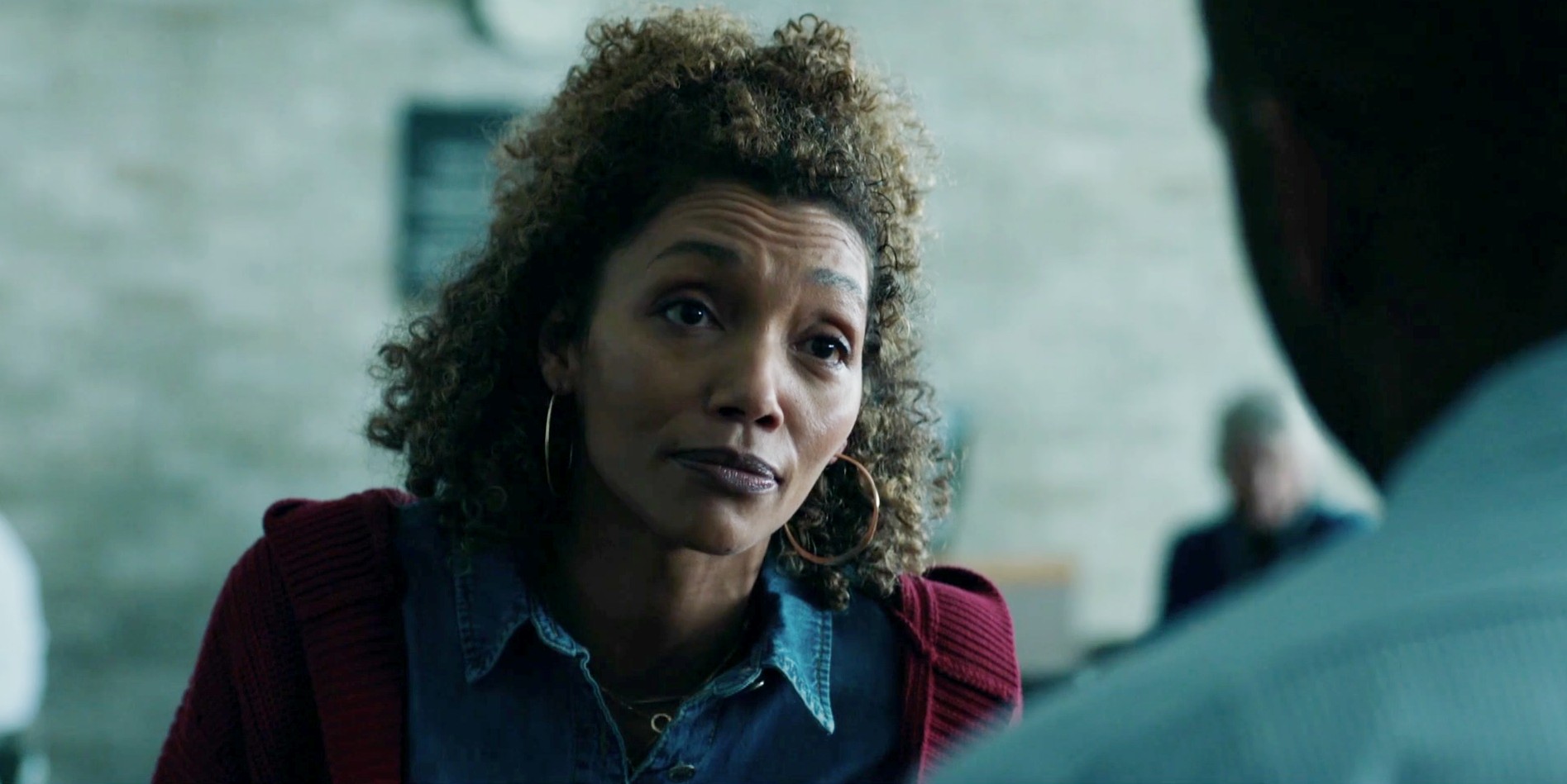 Hopi Grace as Emma in Time. she sits outside in a red cardigan and blue shirt, talking to a family member