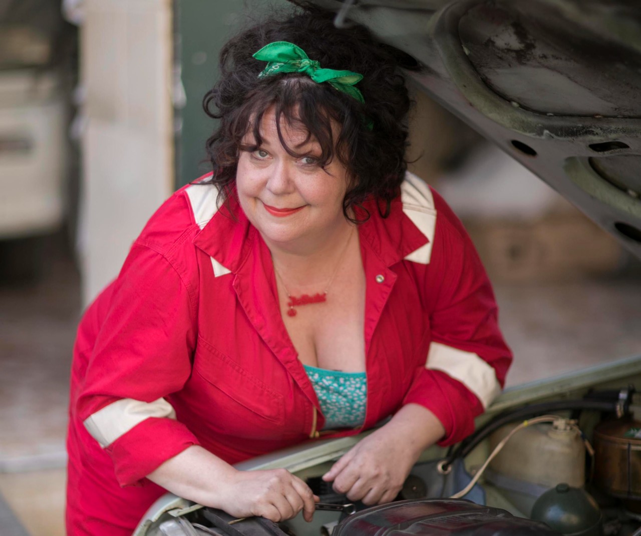 SUE VINCENT AS GLORIA, SHE IS HER MECHANIC UNIFORM SMILING OVER HER CAR IN THE MADAME BLANC MYSTERIES
