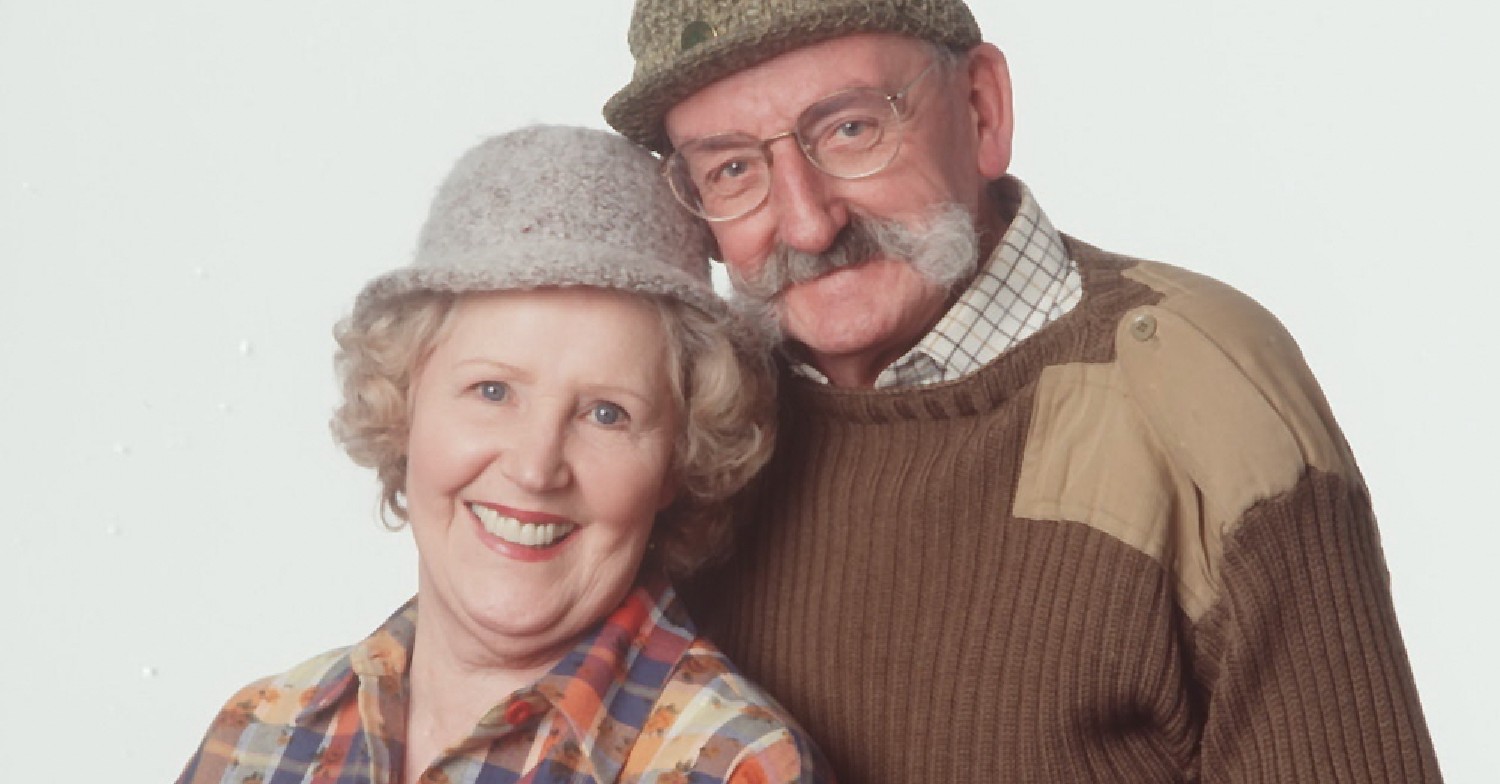 Seth and Betty smiling at camera and both wearing hats Emmerdale 50th anniversary