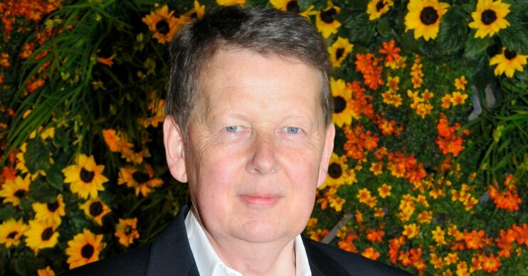 BBC star Bill Turnbull next to a wall of yellow and orange flowers