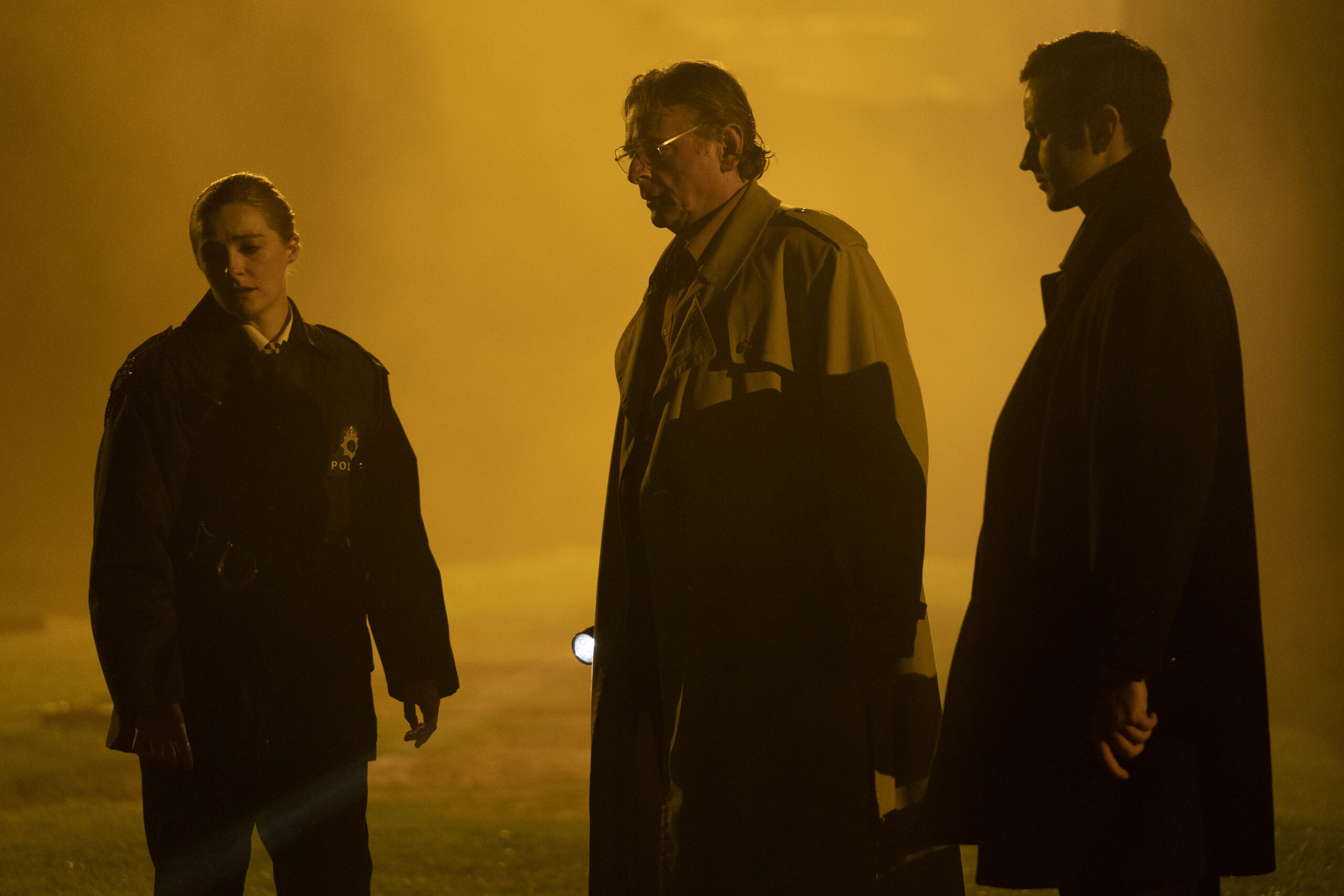 Kevin Mains as DS Jimmy Lawson jr in Karen Pirie, he stands next to Detective McEllihinney and PC Janice Hogg in a foggy graveyard