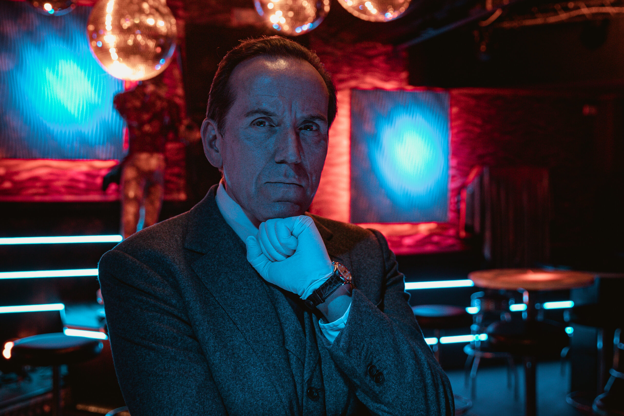 Ben Miller as Professor T, he stands in a crime lab with white gloves on as he stares into the camera
