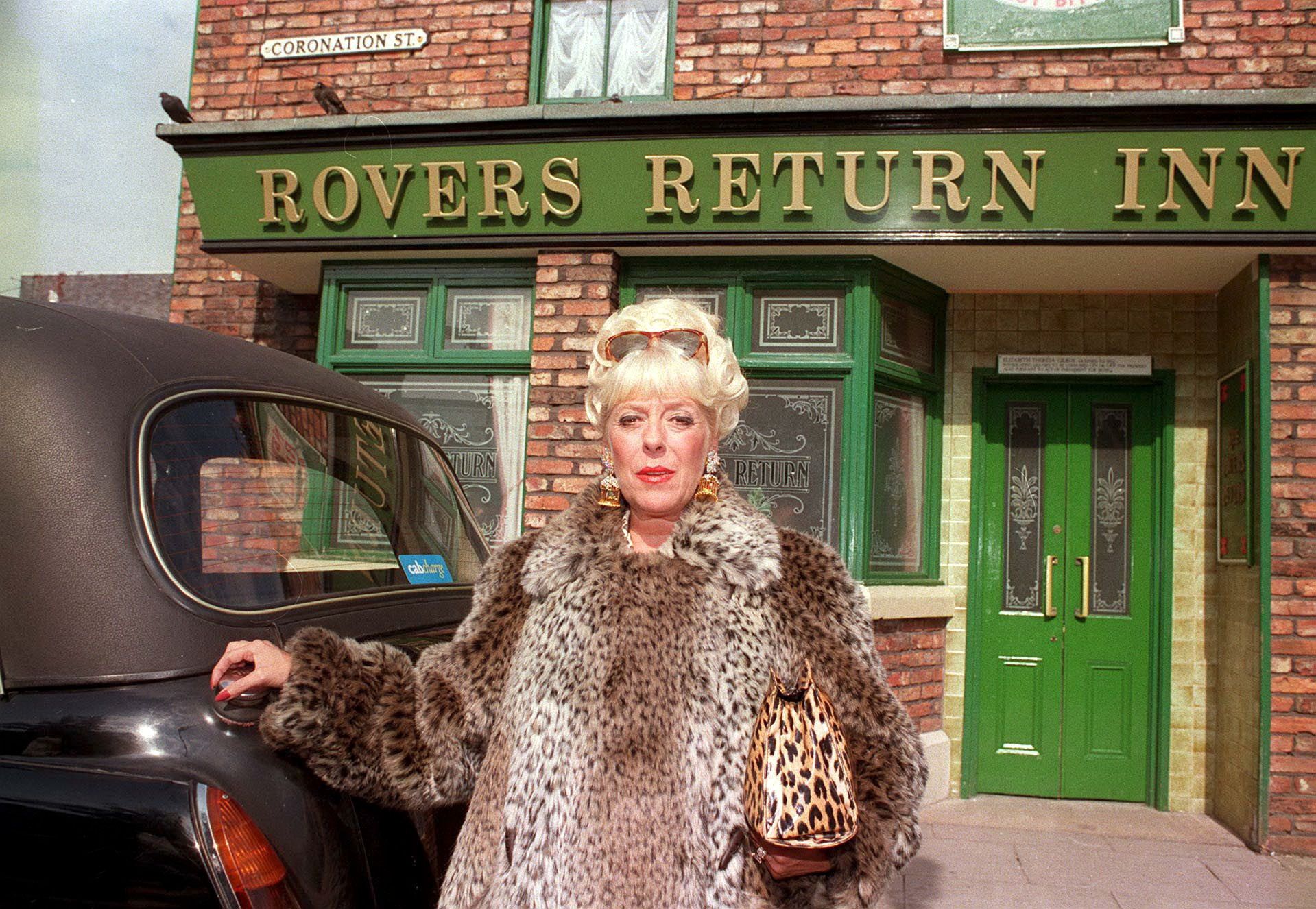 Coronation Street Bet Lynch poses with a taxi outside the Rovers