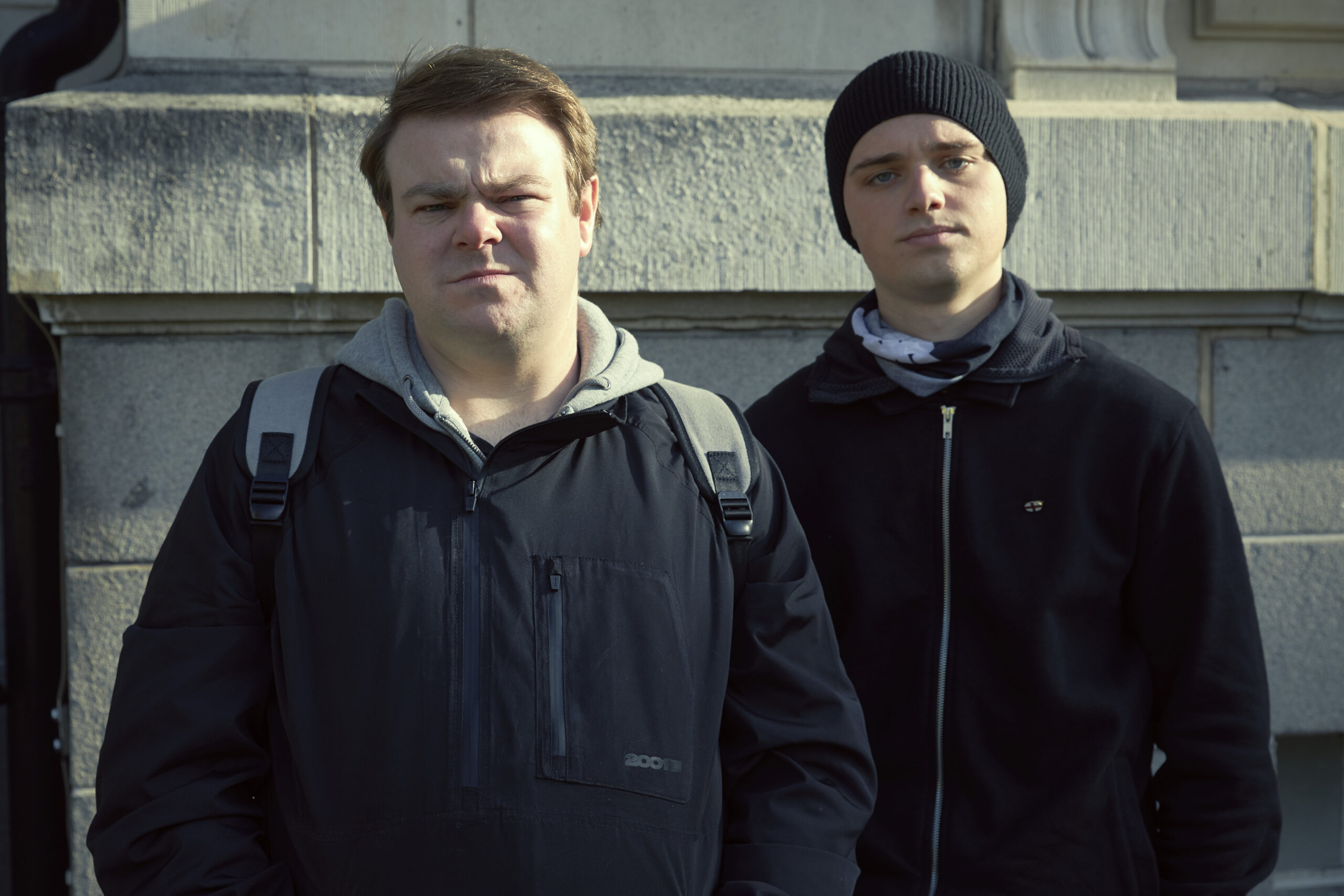 Andrew Ellis as Robbie next to Dean Charles Chapman as Jack, they stand next to each other at a protest, they squint at the camera