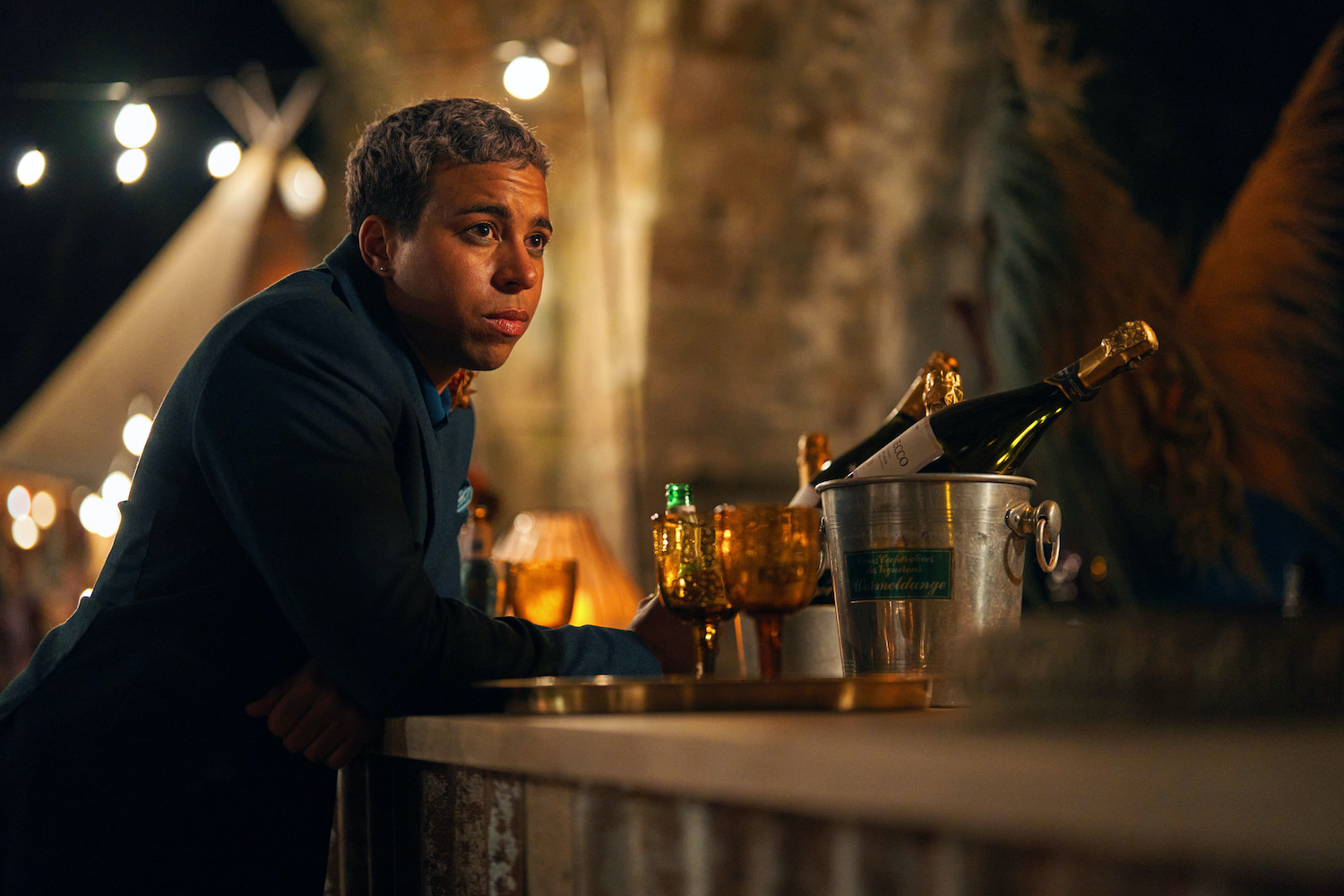Jamie is leaning on a bar looking worried, with a bottle of champagne in an ice bucket in front of him, in The Pact series 2