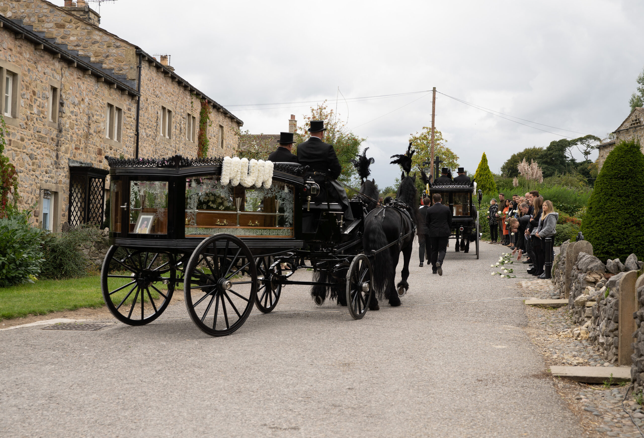 A horse-drawn funeral procession goes through the village, bearing Faith's coffin and flowers