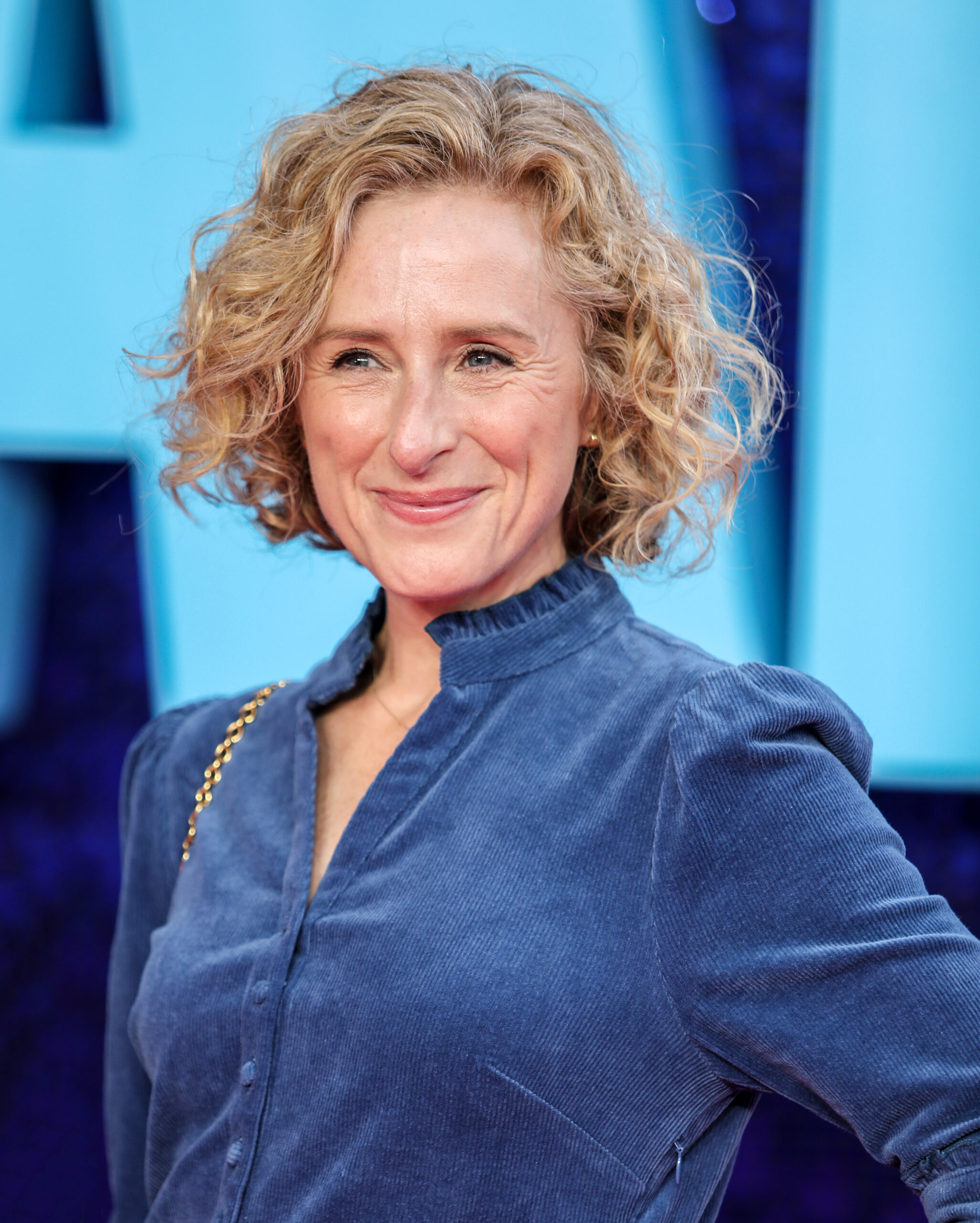 Nicola Stephenson at the premiere of Everybody's Talking About Jamie, she smiles in a blue shirt next to a blue wall