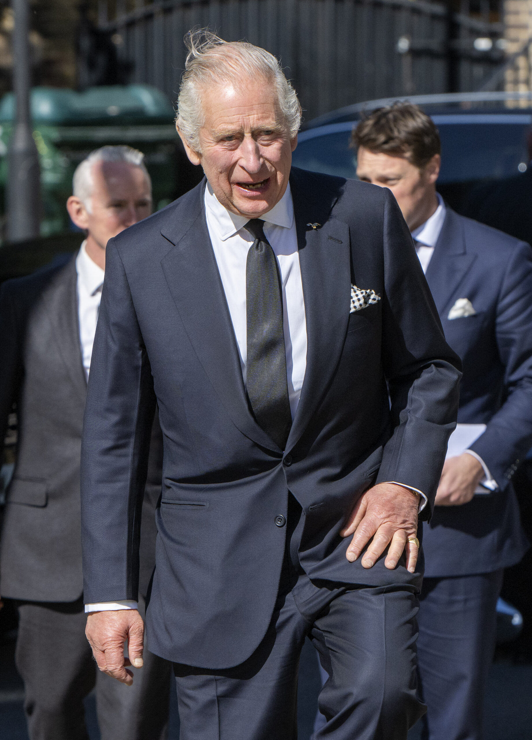 King Charles grimacing in the sunshine in a suit