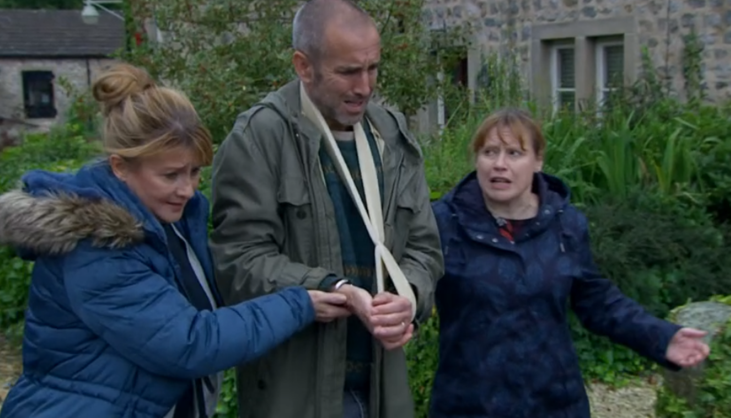 Emmerdale's Sam in a sling, looking upset as he's held up by Wendy and Lydia