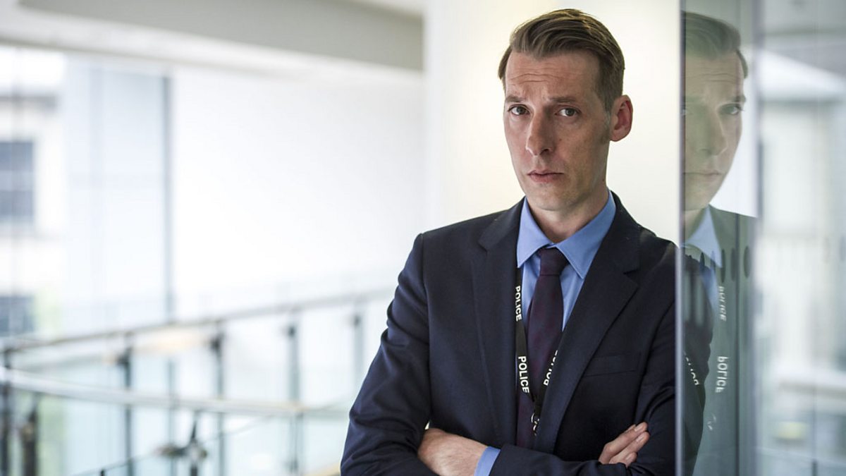 Craig Parkinson as Dot Cottan in Line of Duty, he folds his arms and looks up with a small smile in a large room