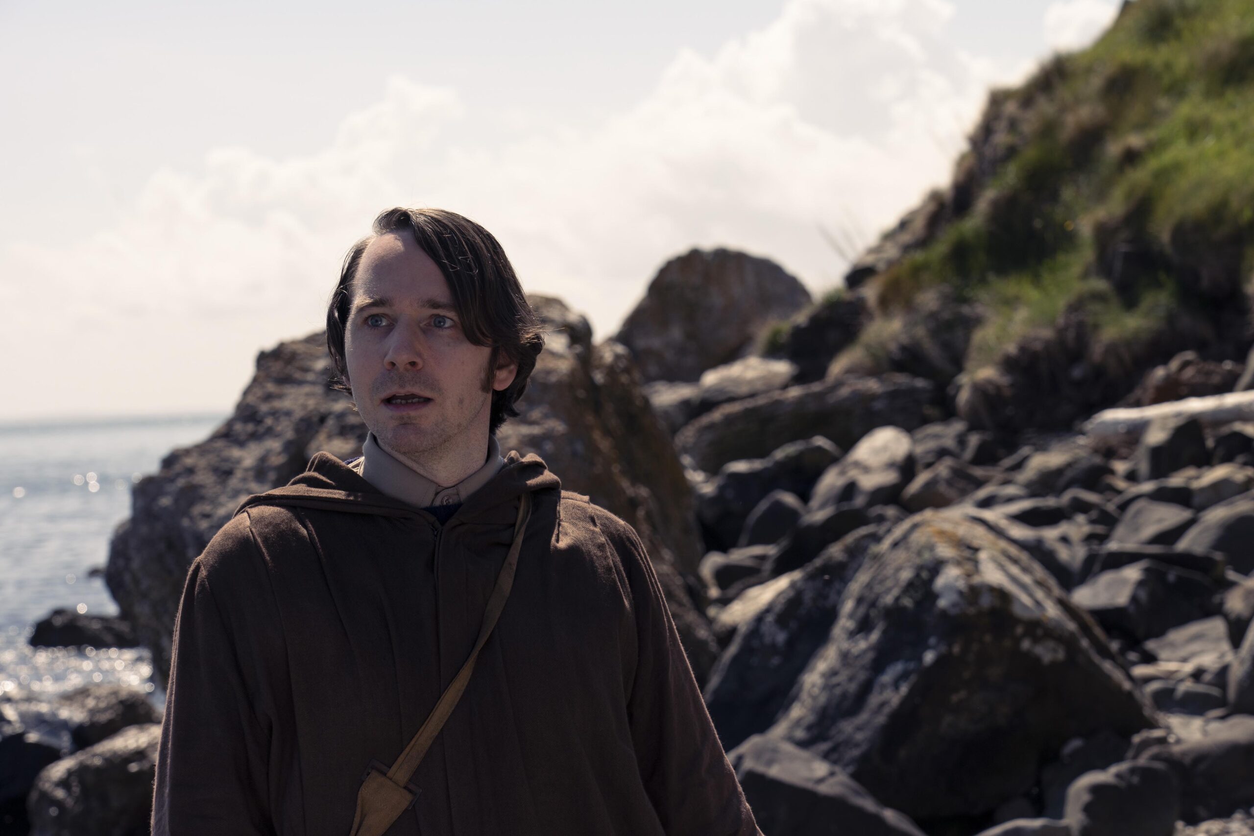 Dennis stands in a robe next to a rocky hilll
